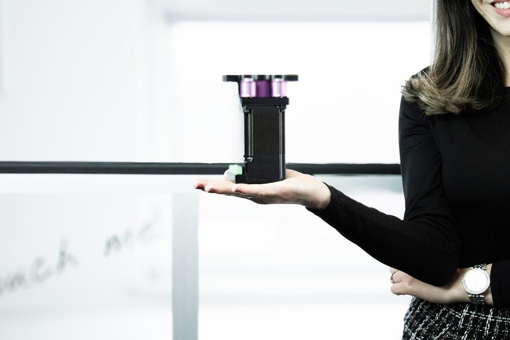 Mitarbeiterin hält energieeffizienten Direktantrieb für eine Hubtür, im Hintergrund eine remonic® MagicGate im Einsatz