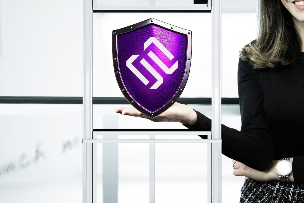 Mitarbeiterin hält ein Schutzschild mit Logo zwischen einer Hubtür als Symbol für Personenschutz und Maschinensicherheit im Maschinen- und Anlagenbau.